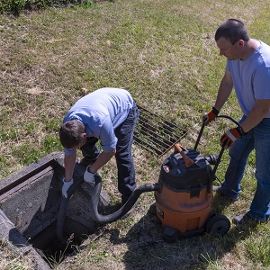 two men at field inlet removing sediment with wet-dry vacuum