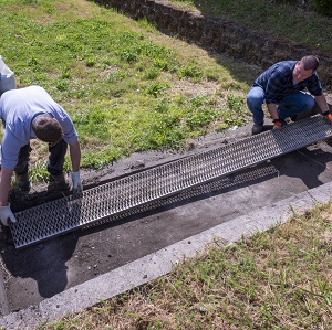 Two men tapping a trash screen against the inside of a sediment trap to remove debris.