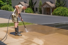 Image of a middle age man pressure washing a driveway.